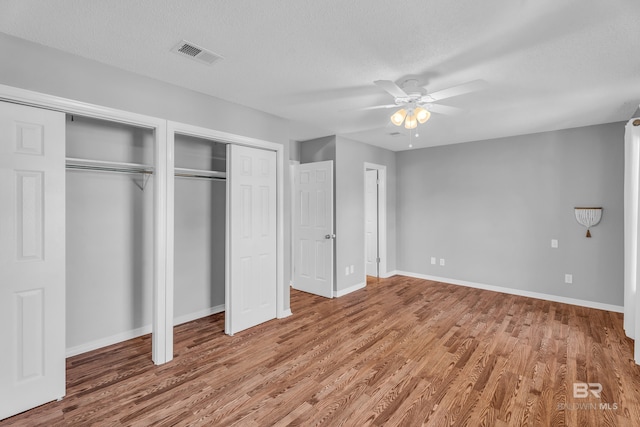 unfurnished bedroom featuring multiple closets, ceiling fan, a textured ceiling, and hardwood / wood-style flooring