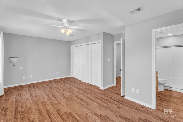 unfurnished bedroom with ensuite bathroom, ceiling fan, light wood-type flooring, a textured ceiling, and multiple closets