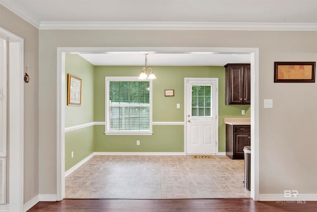 unfurnished dining area with ornamental molding, wood-type flooring, and an inviting chandelier