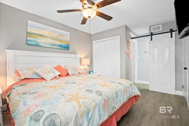 bedroom with a barn door, ceiling fan, a closet, and dark hardwood / wood-style floors