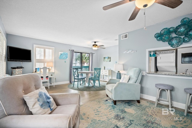 living room with a textured ceiling, light hardwood / wood-style floors, sink, and stacked washer and dryer