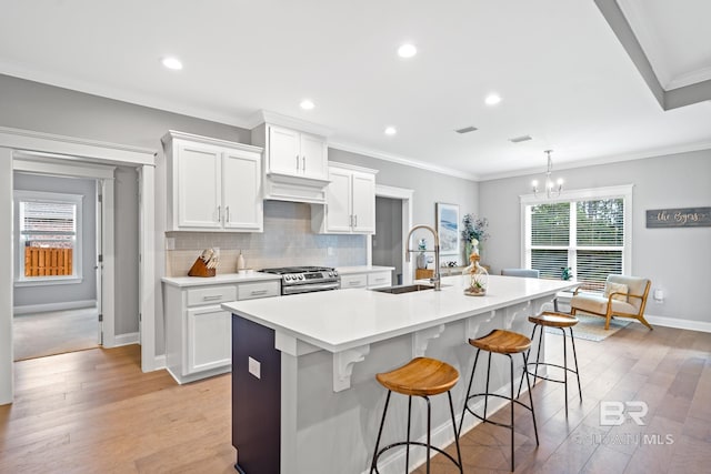 kitchen with white cabinets, pendant lighting, stainless steel range, and an island with sink