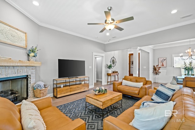 living room featuring ceiling fan with notable chandelier, wood-type flooring, decorative columns, ornamental molding, and a brick fireplace