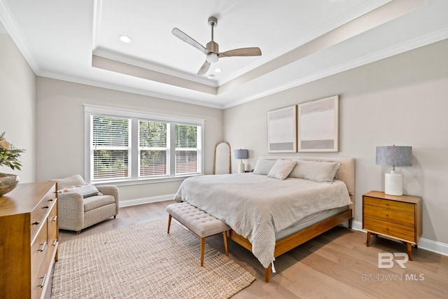 bedroom featuring light wood-type flooring, a tray ceiling, ceiling fan, and ornamental molding