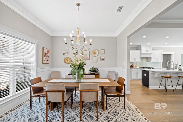 dining room featuring crown molding, light hardwood / wood-style flooring, an inviting chandelier, and sink