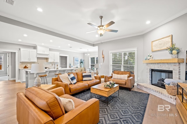 living room with ceiling fan, ornamental molding, light wood-type flooring, and a fireplace