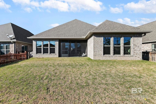 back of property with brick siding, fence, roof with shingles, a lawn, and a sunroom