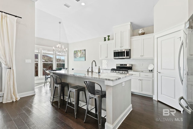 kitchen featuring light stone countertops, dark wood finished floors, stainless steel appliances, decorative backsplash, and vaulted ceiling