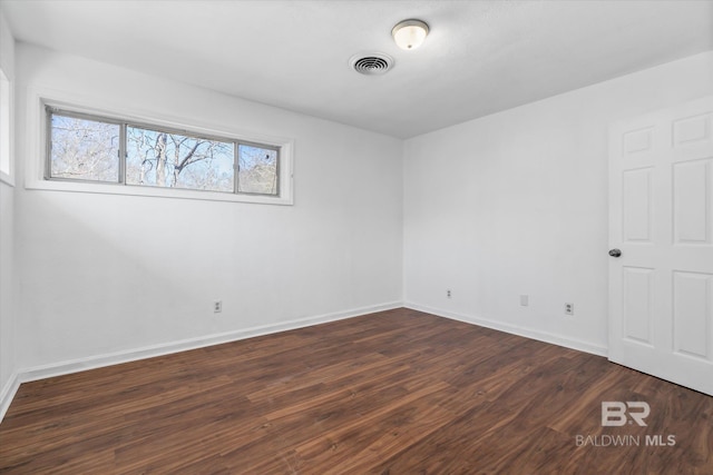 spare room with dark wood finished floors, visible vents, and baseboards