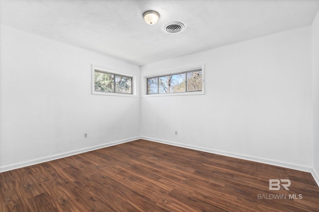 spare room featuring dark wood-style flooring, visible vents, and baseboards