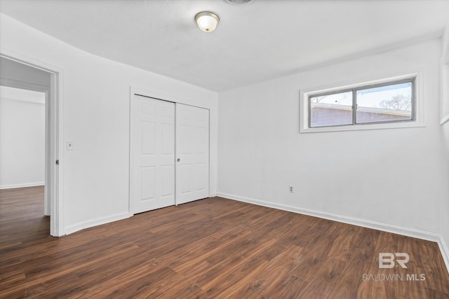 unfurnished bedroom with baseboards, dark wood finished floors, and a closet