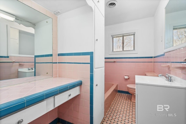 full bathroom with a tub to relax in, visible vents, wainscoting, toilet, and tile walls