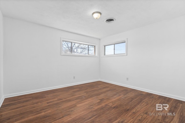 spare room featuring baseboards, visible vents, and dark wood-type flooring