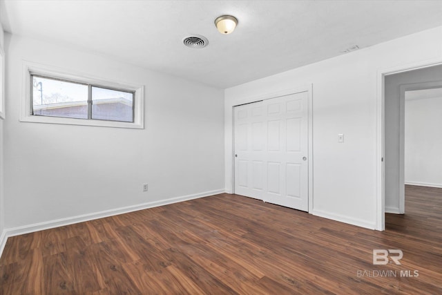 unfurnished bedroom with a closet, visible vents, dark wood finished floors, and baseboards