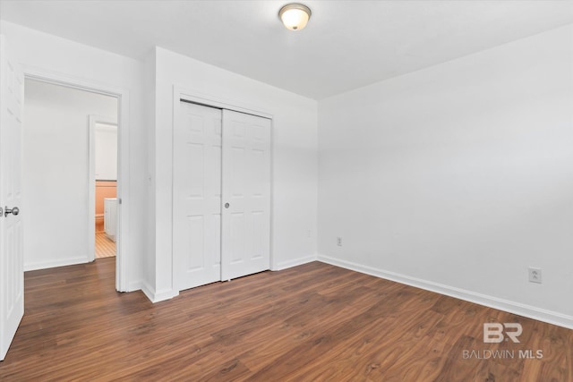 unfurnished bedroom featuring dark wood-style floors, a closet, and baseboards