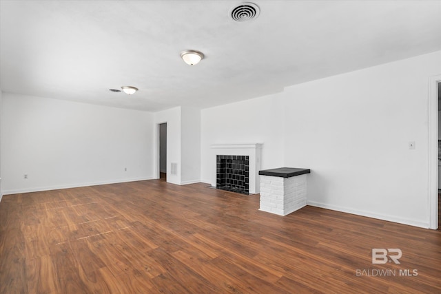 unfurnished living room with a tile fireplace, dark wood-style flooring, visible vents, and baseboards