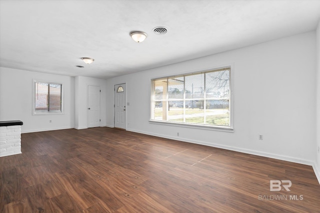 unfurnished living room with dark wood-type flooring, visible vents, and baseboards