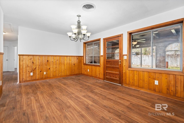 unfurnished dining area featuring a wainscoted wall, visible vents, an inviting chandelier, and wood finished floors