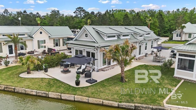 rear view of property featuring metal roof, a water view, a lawn, and a patio area