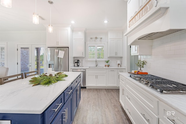 kitchen with blue cabinets, sink, custom range hood, appliances with stainless steel finishes, and white cabinetry