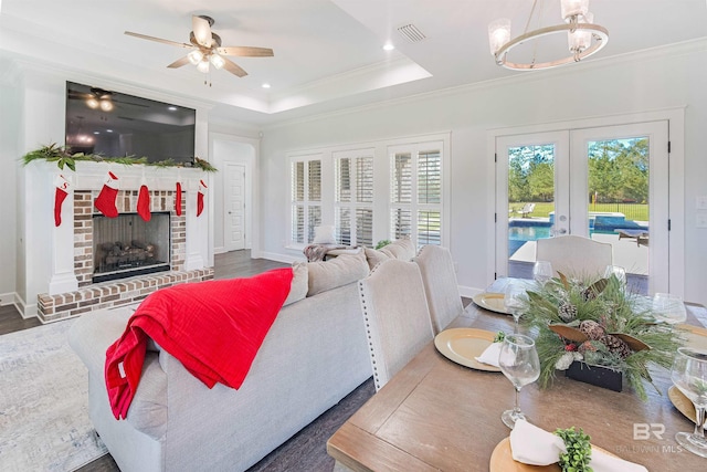 living room with french doors, a raised ceiling, crown molding, dark hardwood / wood-style floors, and a fireplace