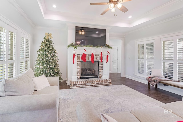 living room with ceiling fan, dark wood-type flooring, a raised ceiling, crown molding, and a fireplace