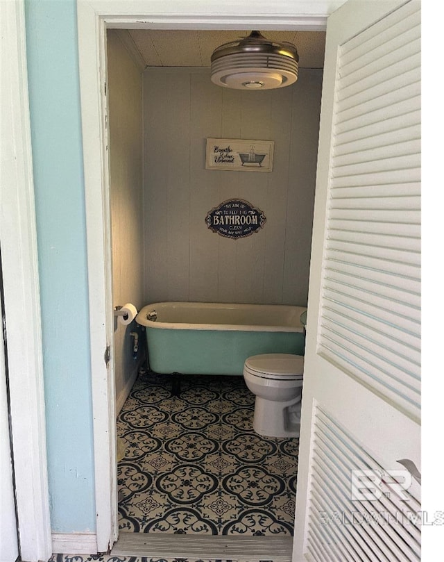 bathroom featuring a bath, toilet, and wood walls