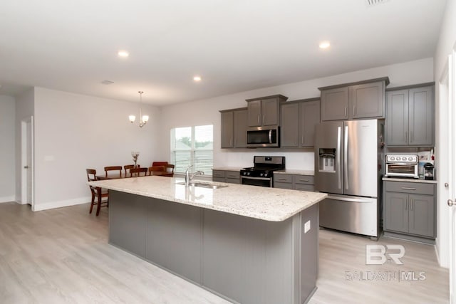 12927 Sanderling Loop, Spanish Fort, AL 36527 - kitchen featuring stainless steel appliances, light wood finished floors, light stone counters, a kitchen island with sink, and hanging light fixtures