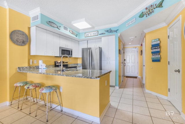 26750 Perdido Beach Blvd Unit 708, Orange Beach, AL 36561 - kitchen with appliances with stainless steel finishes, a peninsula, crown molding, light tile patterned floors, and white cabinetry