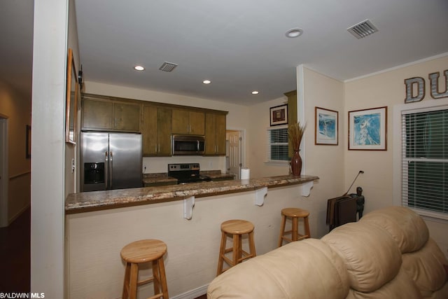 kitchen with a kitchen bar, dark stone countertops, kitchen peninsula, and appliances with stainless steel finishes