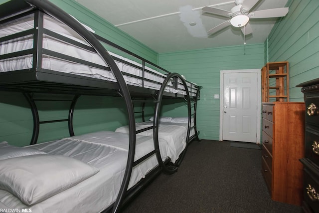 unfurnished bedroom with ceiling fan, wooden walls, dark colored carpet, and vaulted ceiling