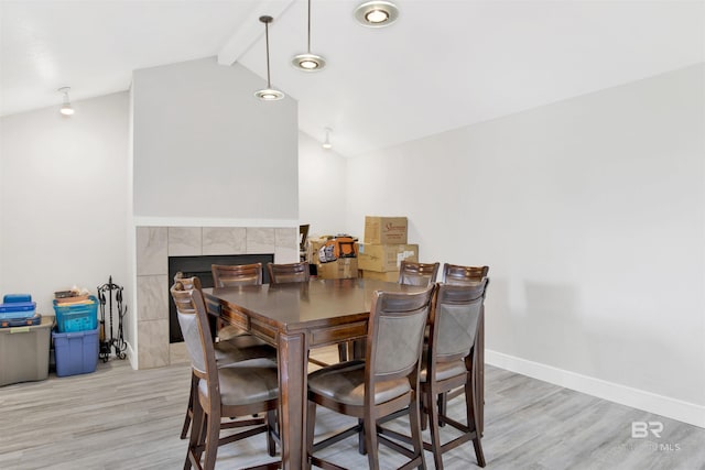 dining room with light wood finished floors, lofted ceiling with beams, baseboards, and a fireplace
