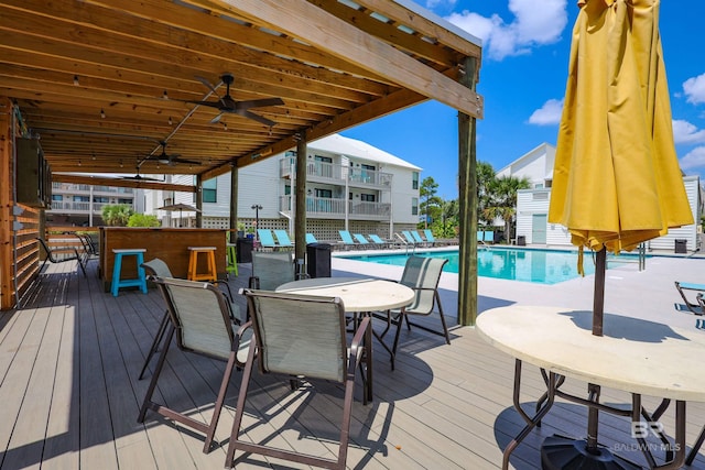wooden terrace featuring a community pool, outdoor dining area, and ceiling fan