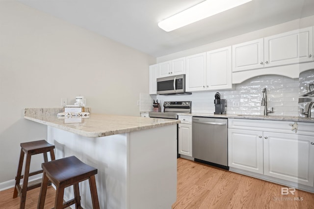 kitchen with a peninsula, white cabinets, appliances with stainless steel finishes, and a kitchen bar