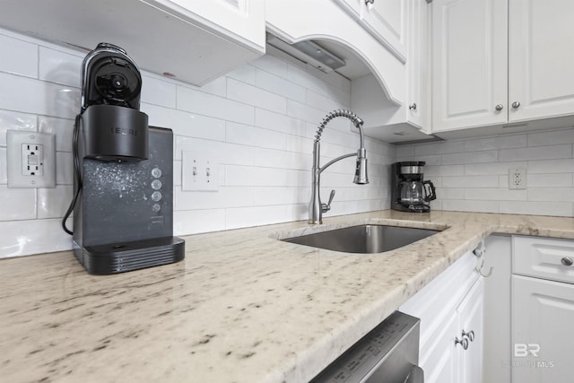 kitchen with a sink, tasteful backsplash, white cabinetry, and light stone countertops