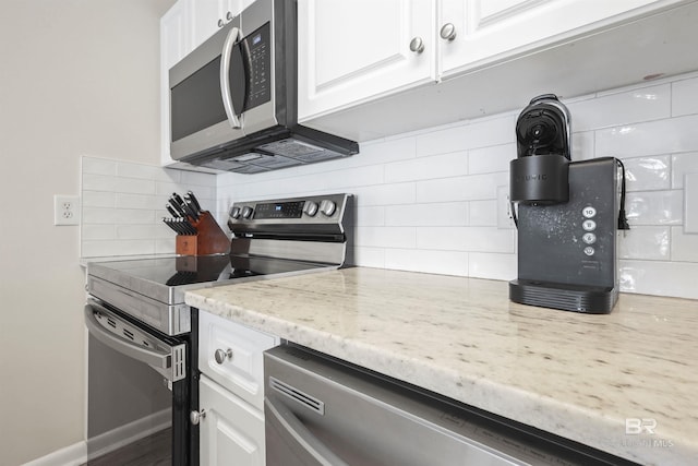 kitchen featuring baseboards, white cabinets, light stone countertops, decorative backsplash, and appliances with stainless steel finishes