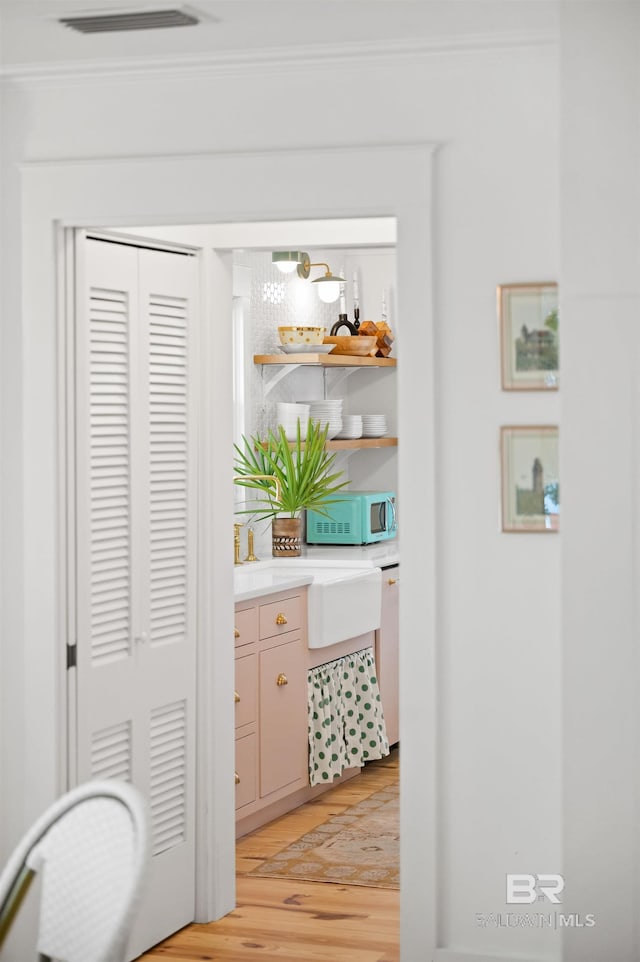 hall featuring crown molding, visible vents, and light wood-style flooring