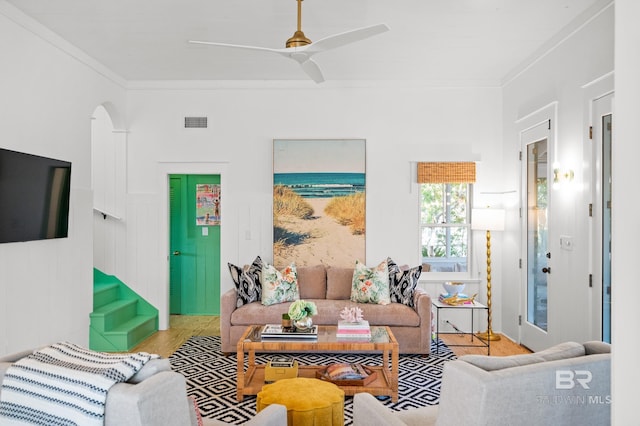living area with ornamental molding, stairs, visible vents, ceiling fan, and arched walkways