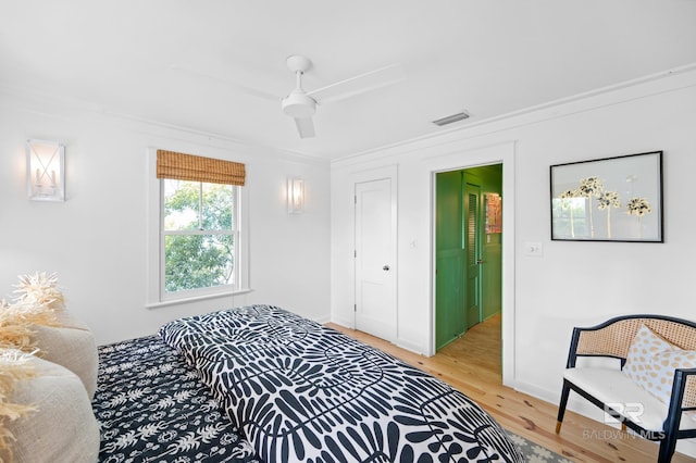 bedroom featuring baseboards, light wood-style flooring, crown molding, a ceiling fan, and visible vents