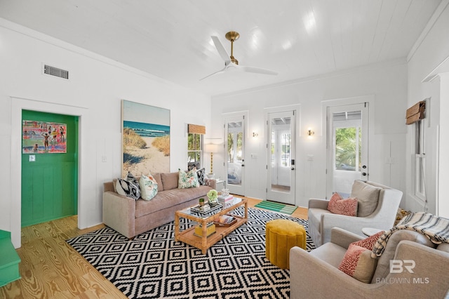 living room featuring a ceiling fan, light wood-type flooring, ornamental molding, and visible vents