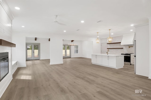 unfurnished living room featuring a large fireplace, french doors, light wood-type flooring, and recessed lighting