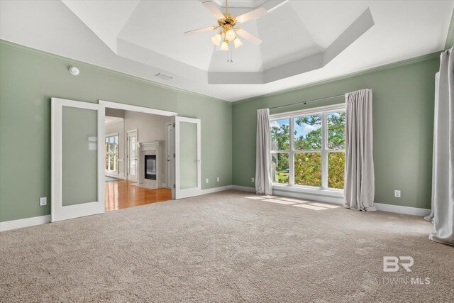 unfurnished bedroom with light carpet, a tray ceiling, ceiling fan, and a high end fireplace