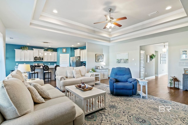 living room featuring hardwood / wood-style floors, a tray ceiling, ornamental molding, and ceiling fan