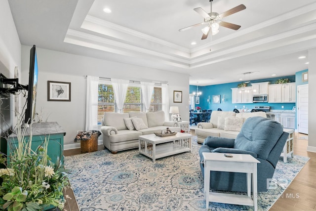 living room featuring ceiling fan, ornamental molding, a tray ceiling, and light hardwood / wood-style floors