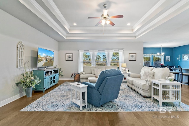 living room featuring a tray ceiling, wood-type flooring, ornamental molding, and ceiling fan with notable chandelier