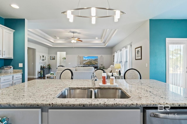 kitchen with sink, hanging light fixtures, white cabinets, a center island with sink, and a raised ceiling