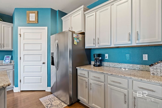 kitchen with stainless steel refrigerator with ice dispenser, light hardwood / wood-style flooring, light stone counters, and white cabinets