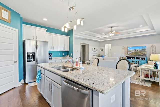 kitchen with sink, appliances with stainless steel finishes, a tray ceiling, a kitchen island with sink, and white cabinets