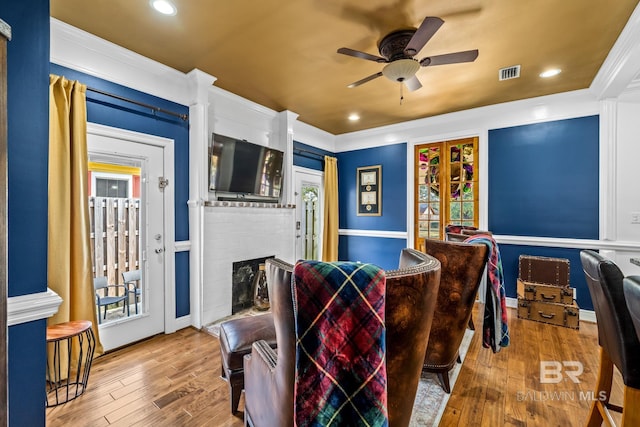 interior space featuring ceiling fan, ornamental molding, a fireplace, and light hardwood / wood-style floors