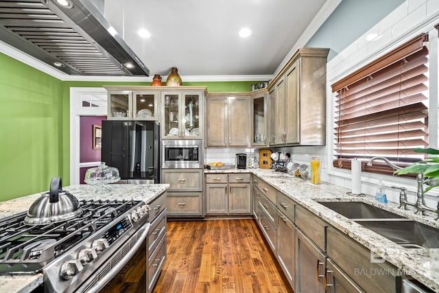 kitchen with crown molding, backsplash, stainless steel appliances, light stone countertops, and wall chimney range hood